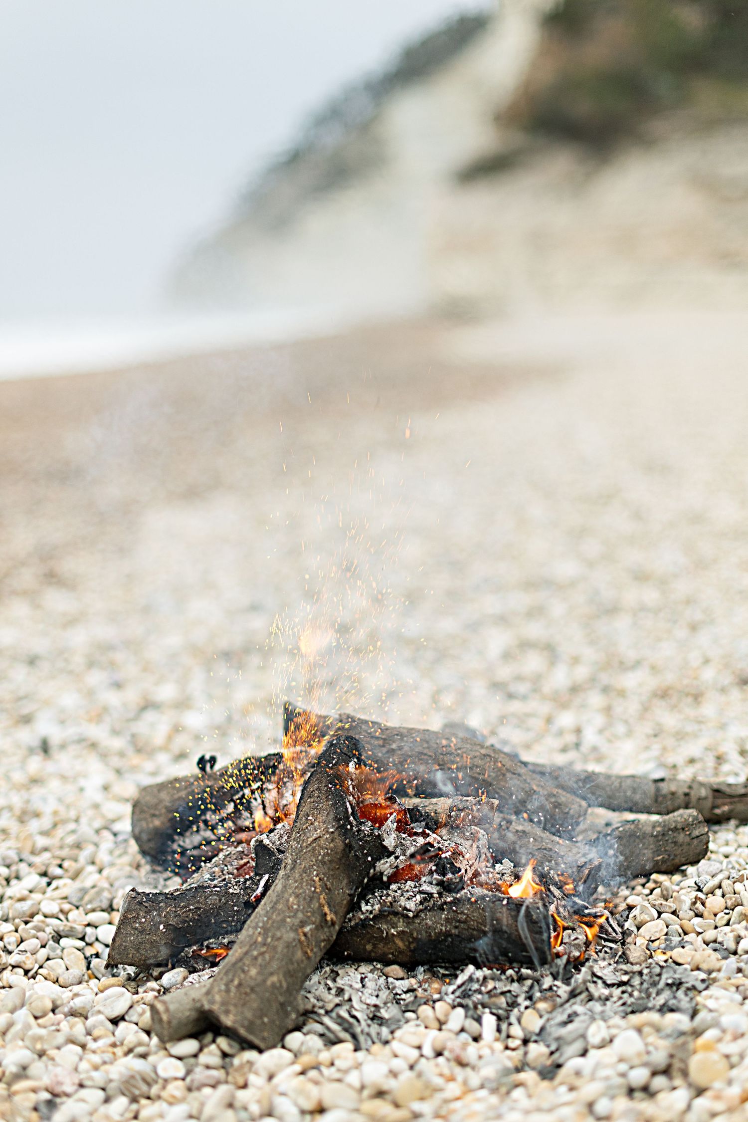 Smoldering campfire logs on a rocky beach.