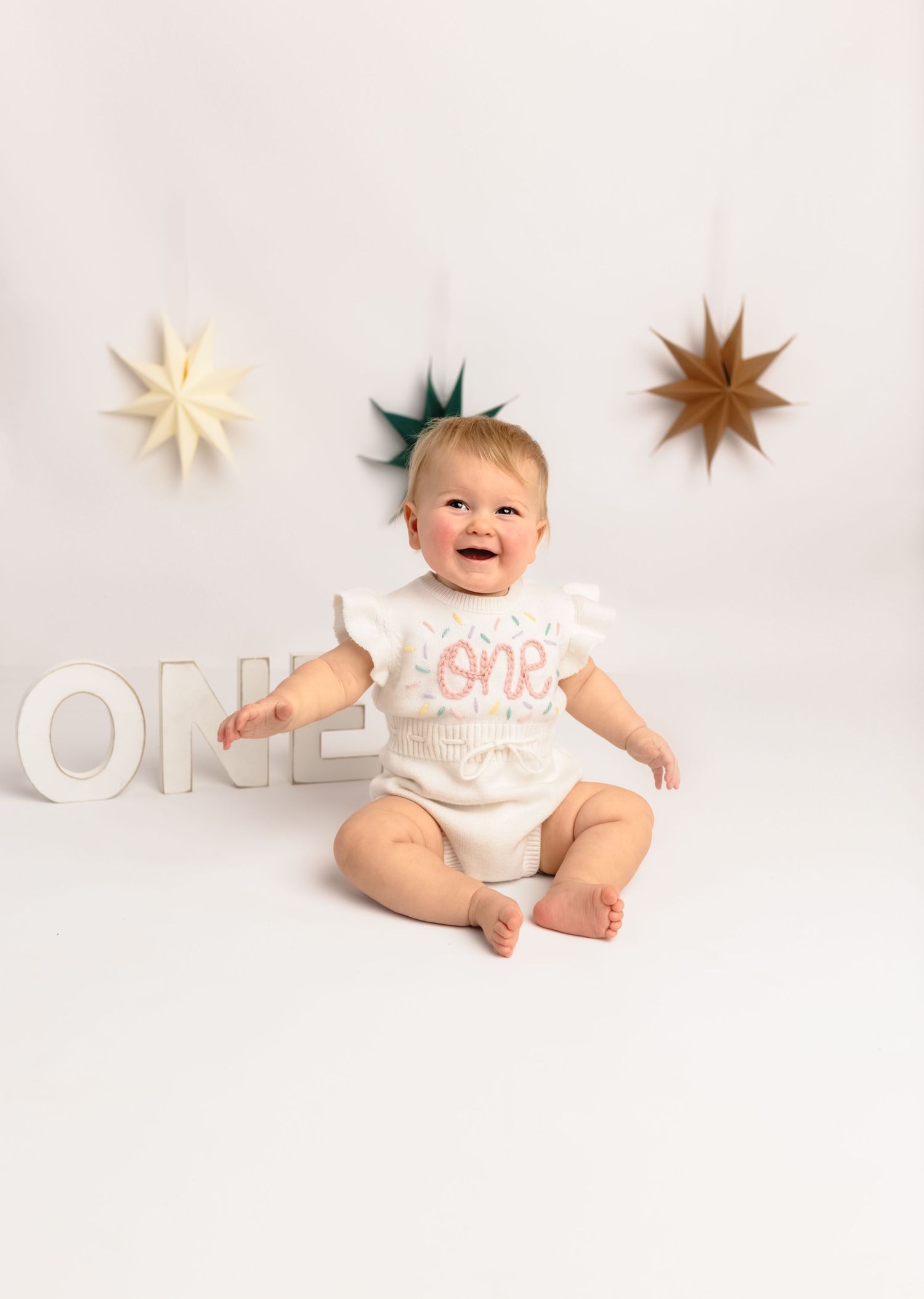 Minimalist cake smash portrait of baby girl wearing 'one' romper on white backdrop at Charlottesville studio.