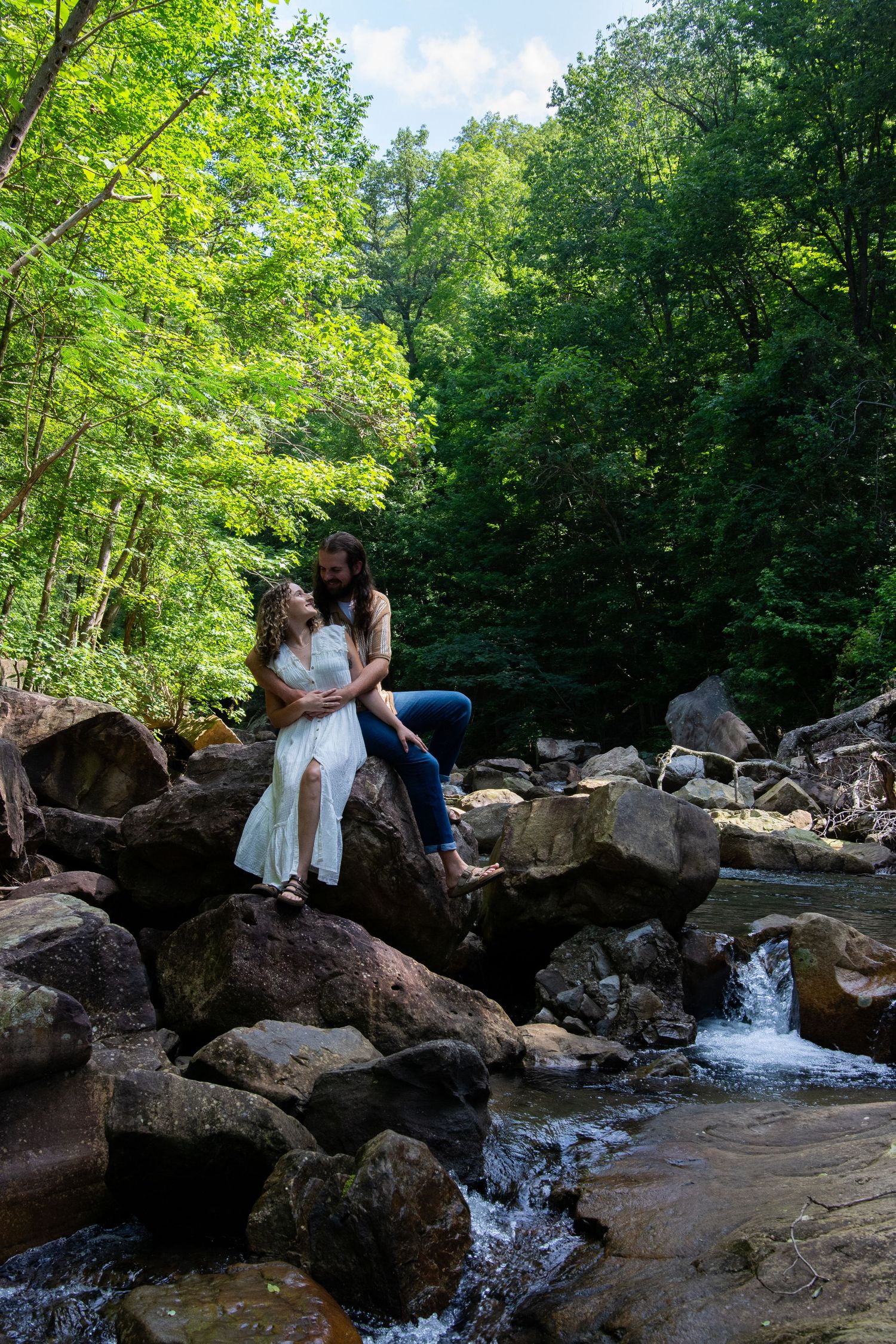 A couple in coordinated spring outfits poses by a river under a bridge wearing white and blue clothing.