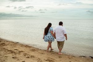 A couple walks hand in hand along the shore with gentle waves lapping at the tropical beach during sunset.