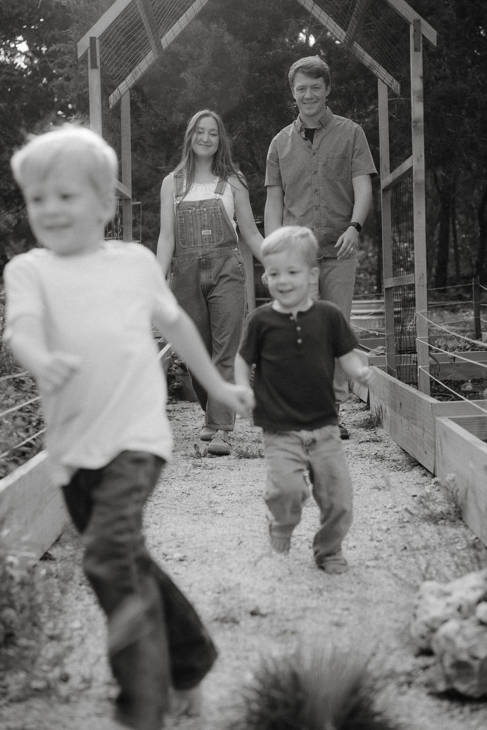 A series of black and white photos showing people interacting with toddlers around raised garden beds with wooden structures.