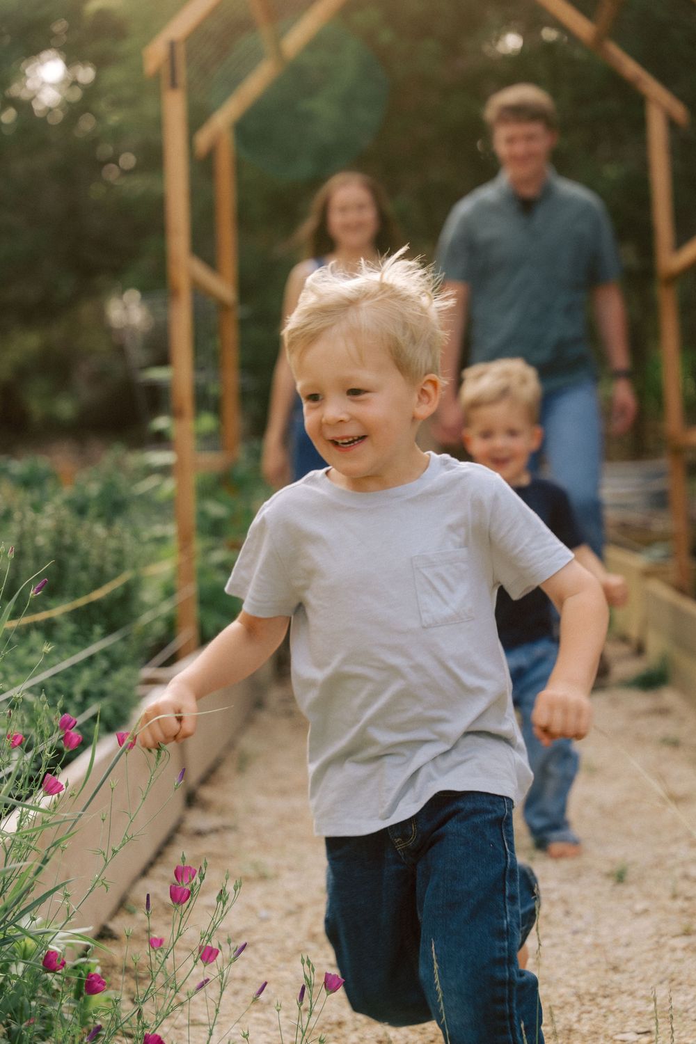 Young child running along a garden path surrounded by pink flowers with a wooden archway in the background.