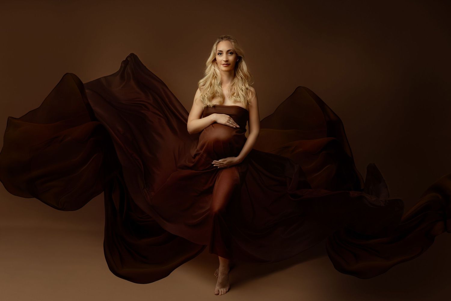 Artistic maternity photos with flowing brown fabric creating dramatic movement against dark background.