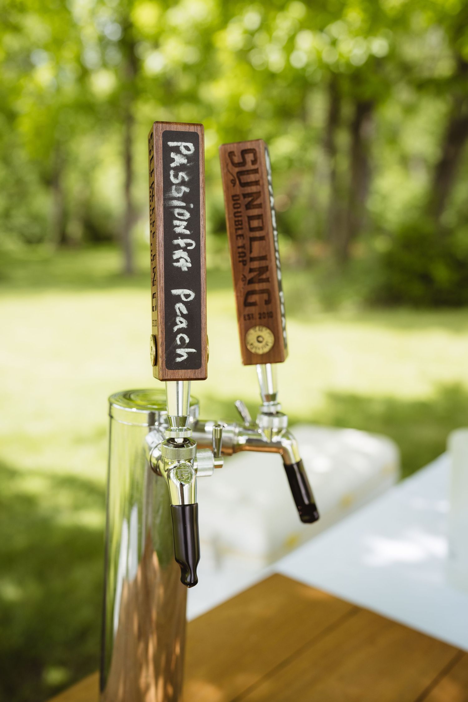 Beer tap handles with rustic wooden designs mounted on a bar outdoors with green foliage in the background.