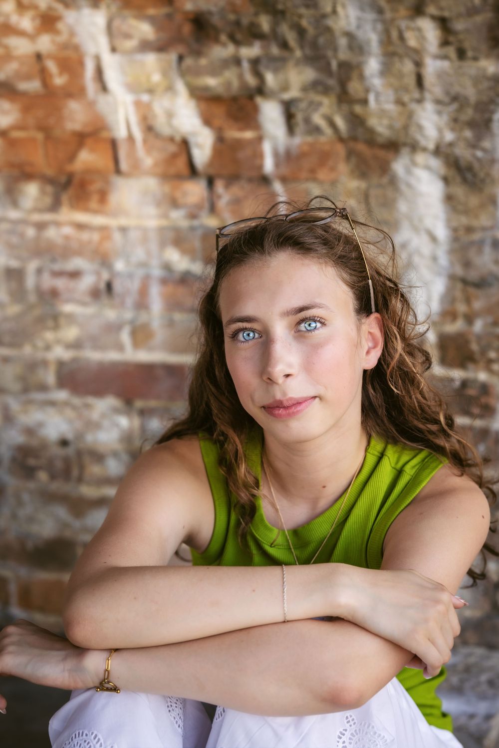 Youth in bright green sleeveless top poses casually against rustic brick wall in artistic portrait series.