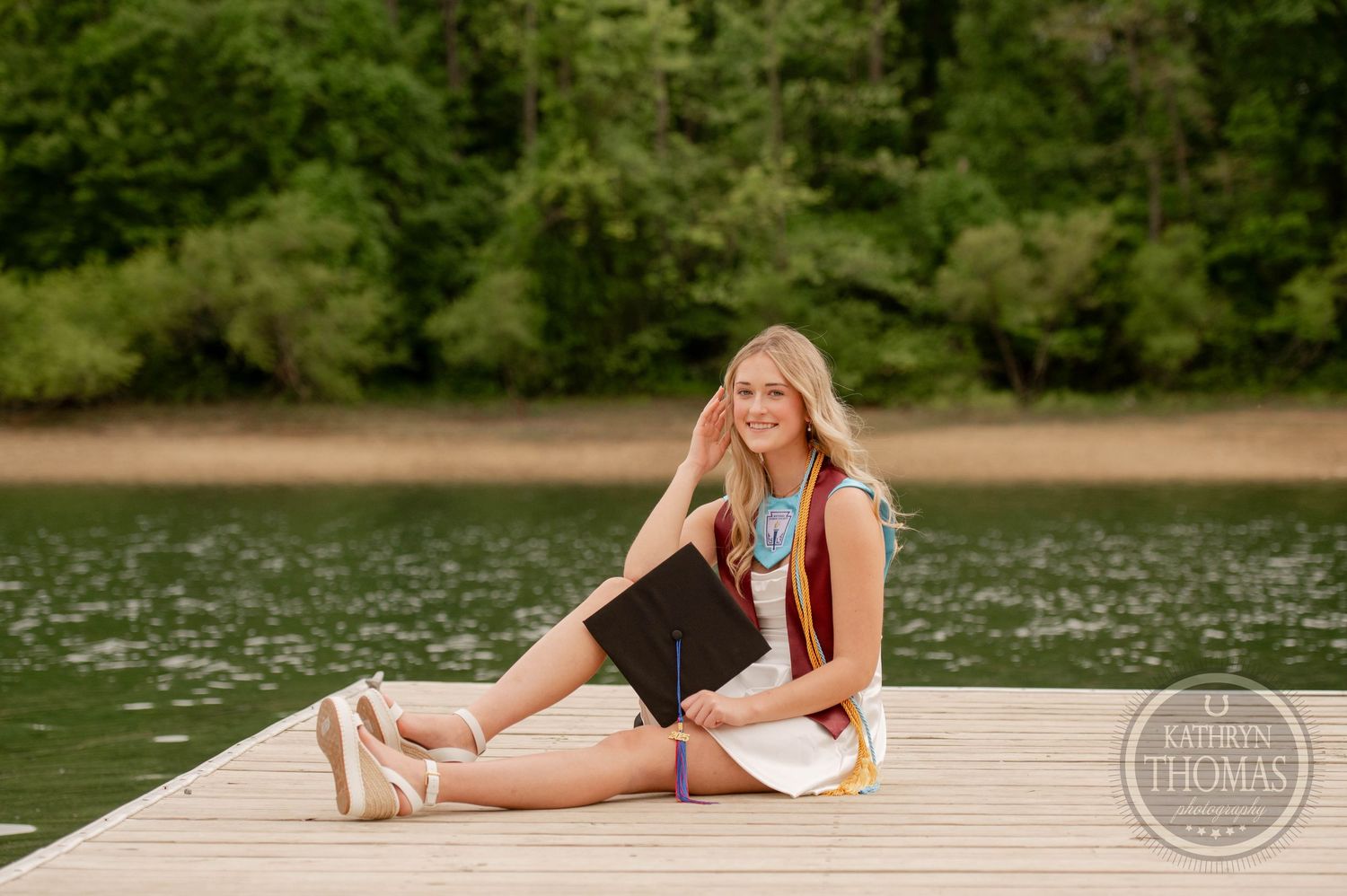 Someone relaxing on a wooden dock by a serene lake on a summer day with trees in the background.