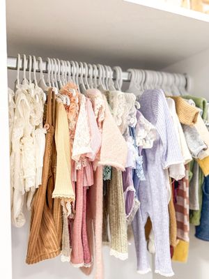Clothing rack displaying pastel and neutral-toned baby clothes hanging neatly on white hangers.