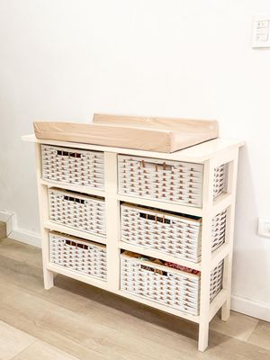 White storage cabinet with woven baskets displayed in different stages of assembly against a light wall.
