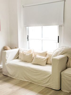 Comfortable white slipcovered sofa with plush pillows against a bright window.
