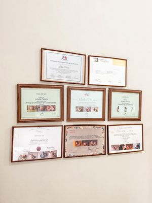 Collection of framed certificates and professional credentials displayed on beige wall.