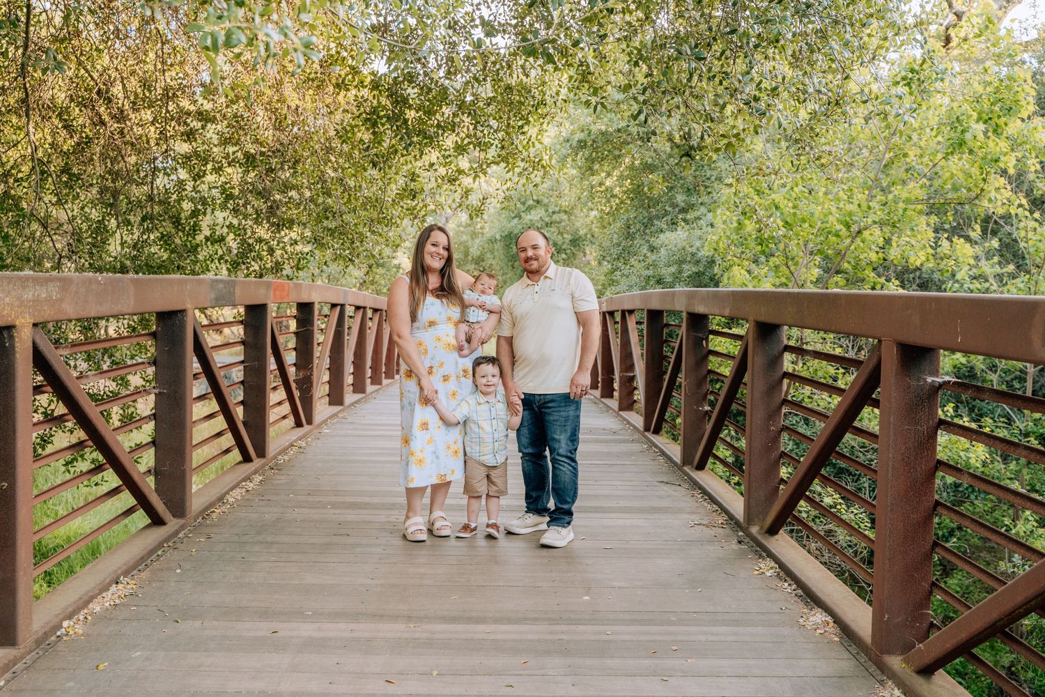 People walking across rustic wooden bridge path surrounded by green trees.