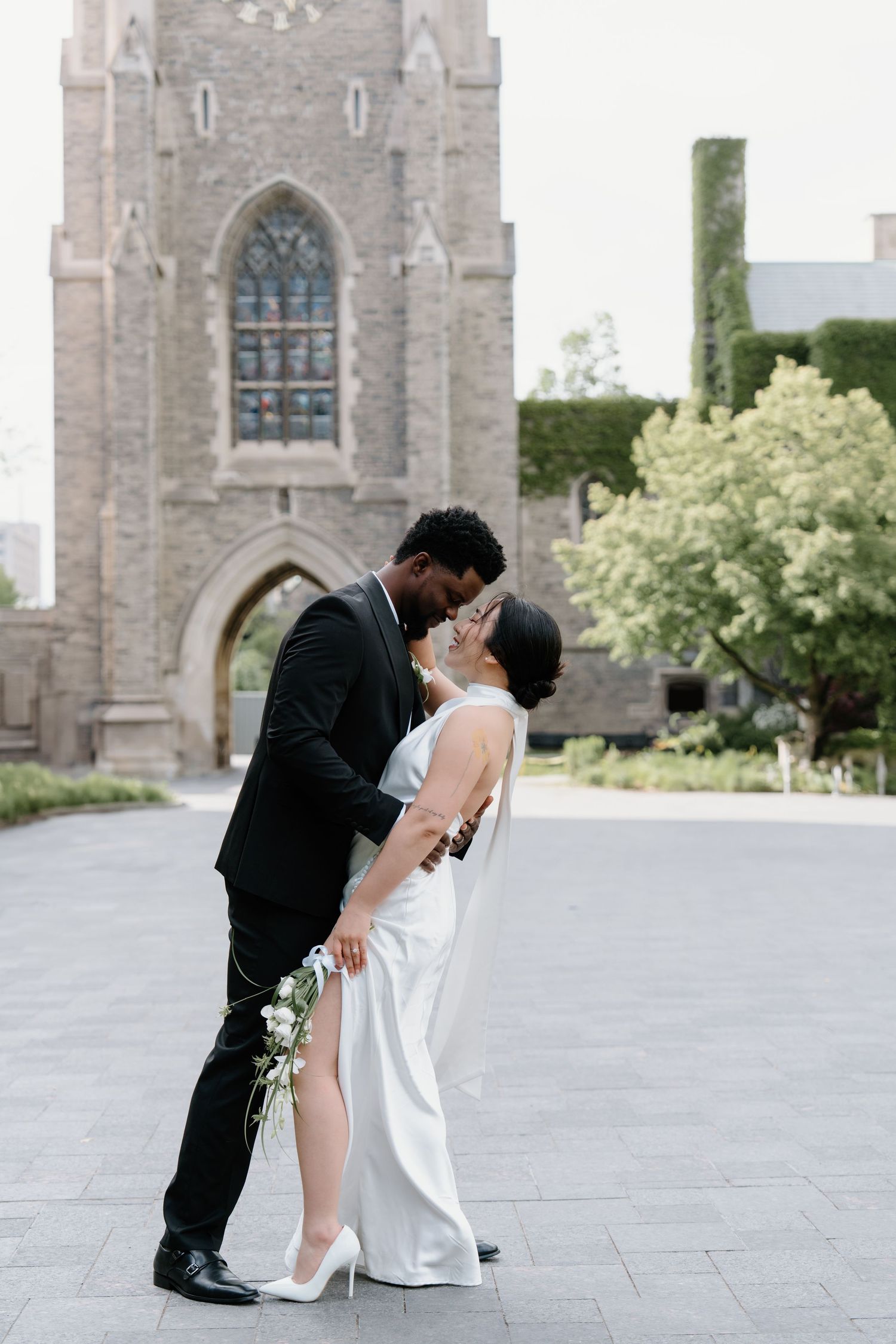 A romantic wedding couple shares an intimate moment in front of a gothic church with stained glass windows.