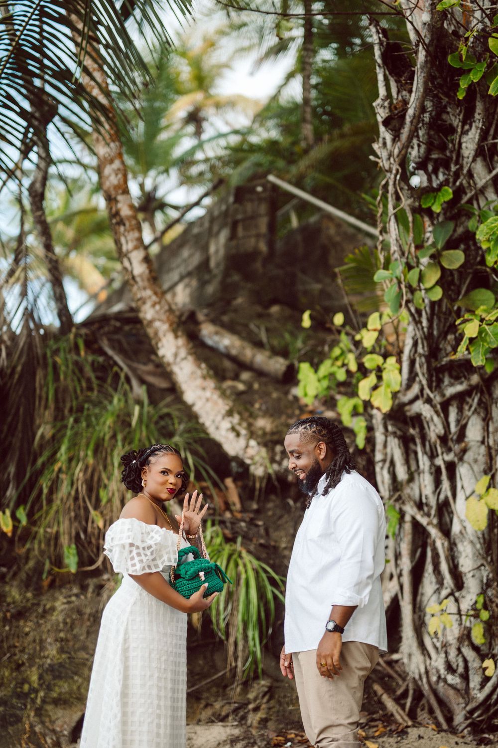 Couple sharing a romantic moment in tropical setting with palm trees and greenery in the background.