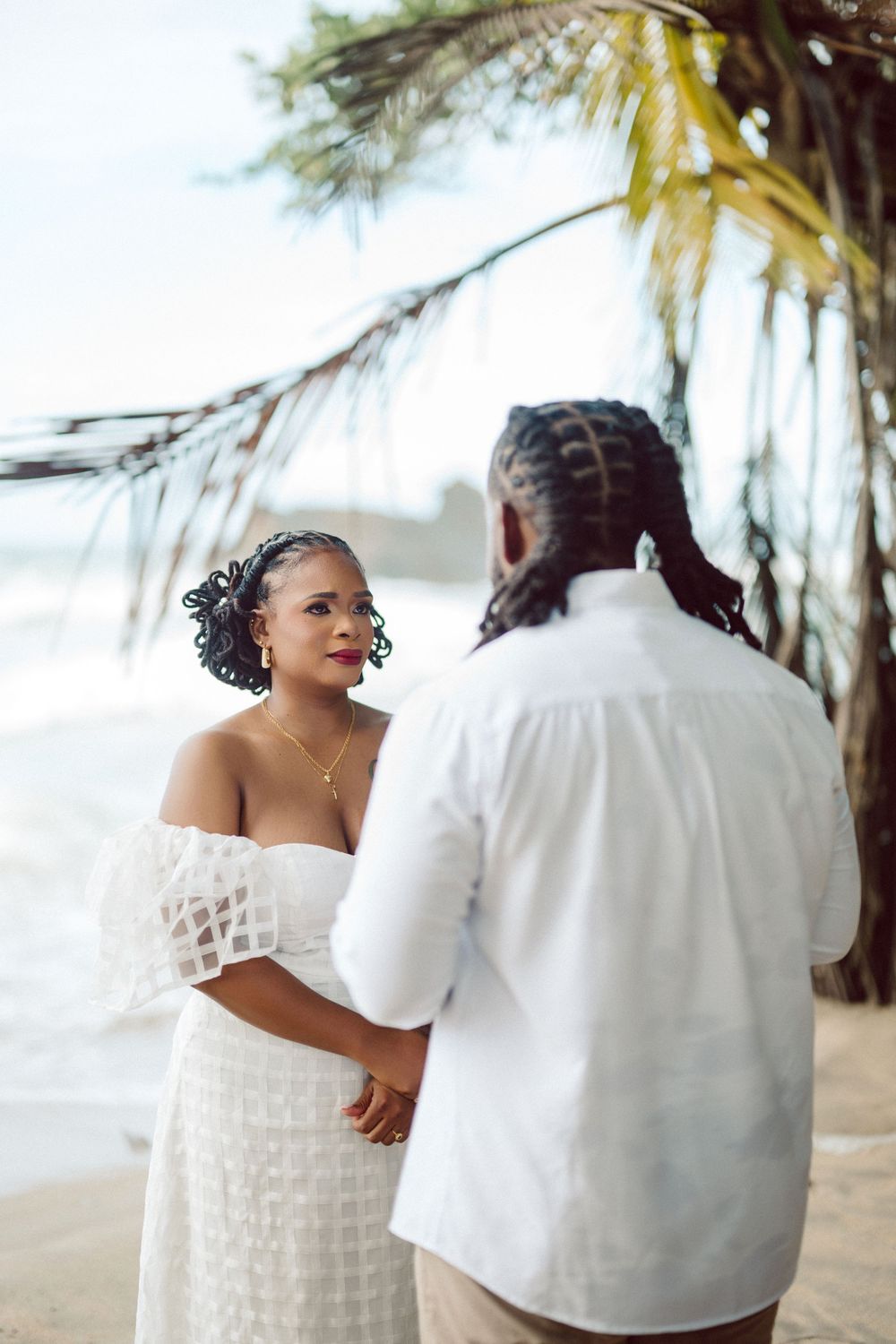 A couple in wedding attire share intimate moments on a tropical beach with palm trees in the background.