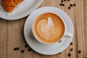 Overhead view of a latte with artistic leaf design in foam on wooden table.