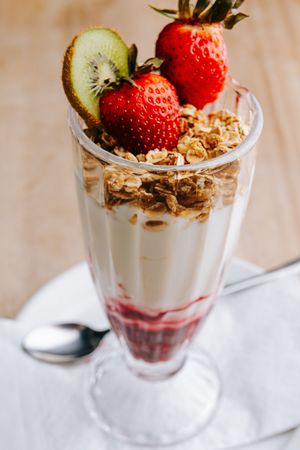 A layered yogurt parfait with fresh strawberries, kiwi slices and granola in a clear glass, photographed from multiple angles.