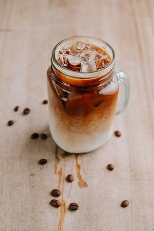 Iced coffee drinks with layered cream and coffee beans scattered on a light surface.