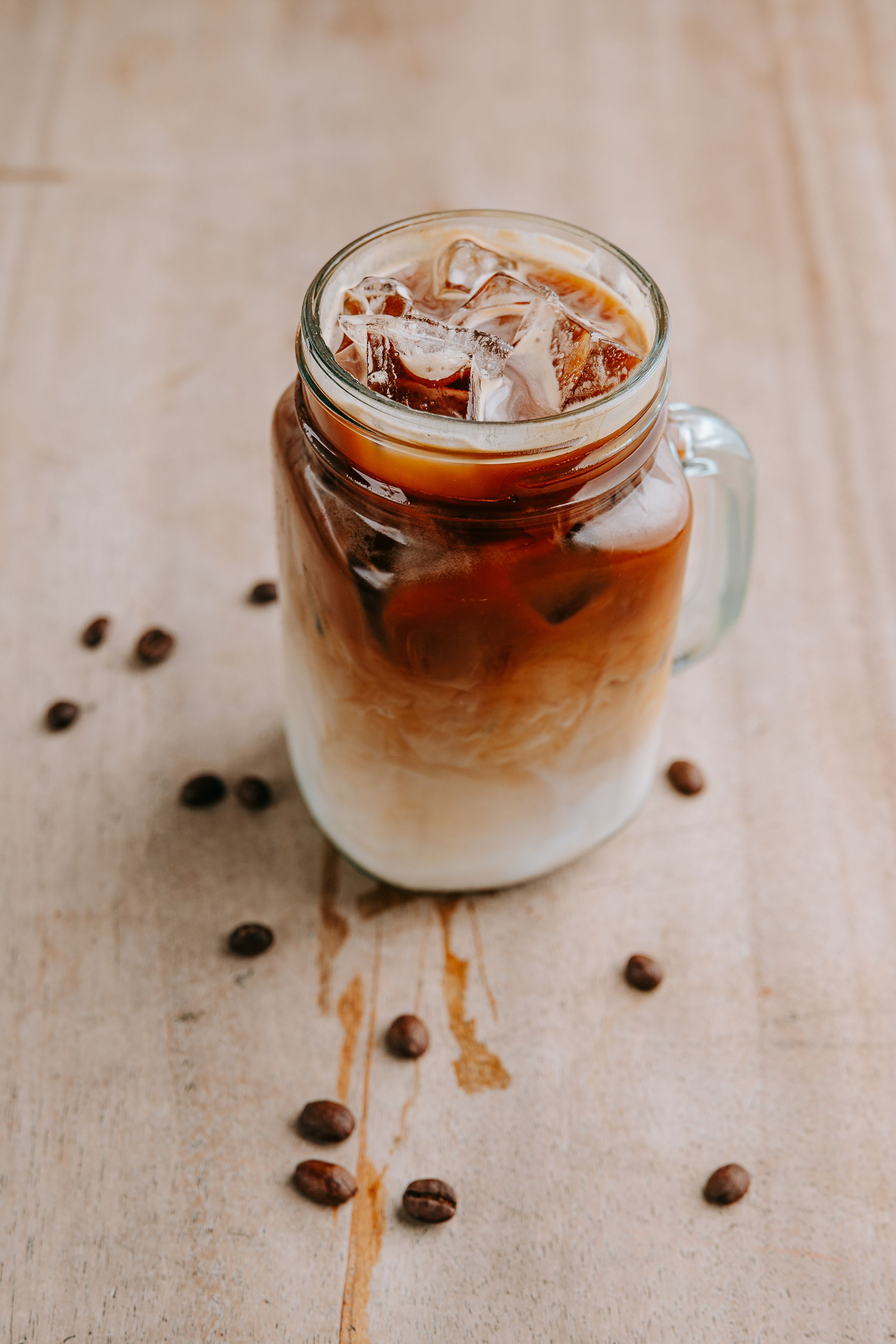 Iced coffee drinks with layered cream and coffee beans scattered on a light surface.
