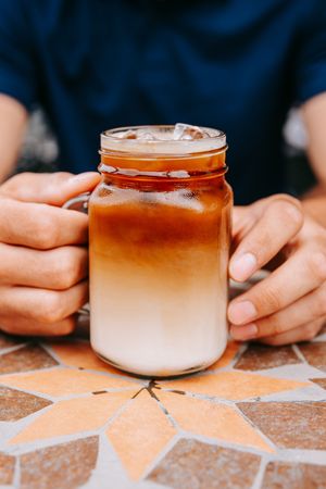 A sequence of hands holding ombre-colored iced coffee drinks in mason jars on a patterned surface.