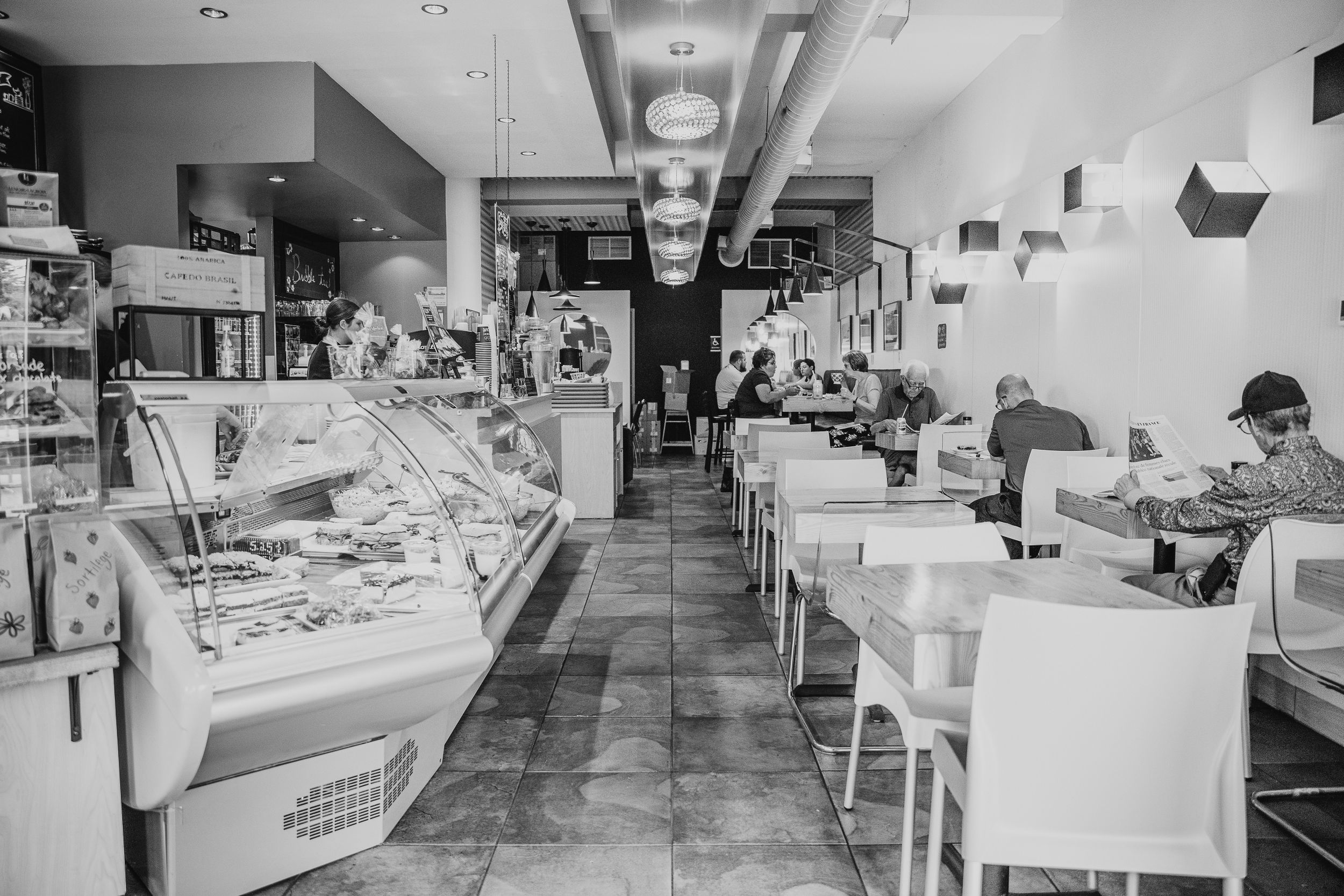 Black and white photograph of vintage diner interior with counter seating and display cases.