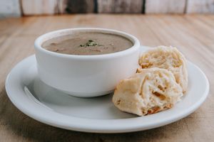A close-up view of creamy mushroom soup served in a white bowl with a side of crusty bread.