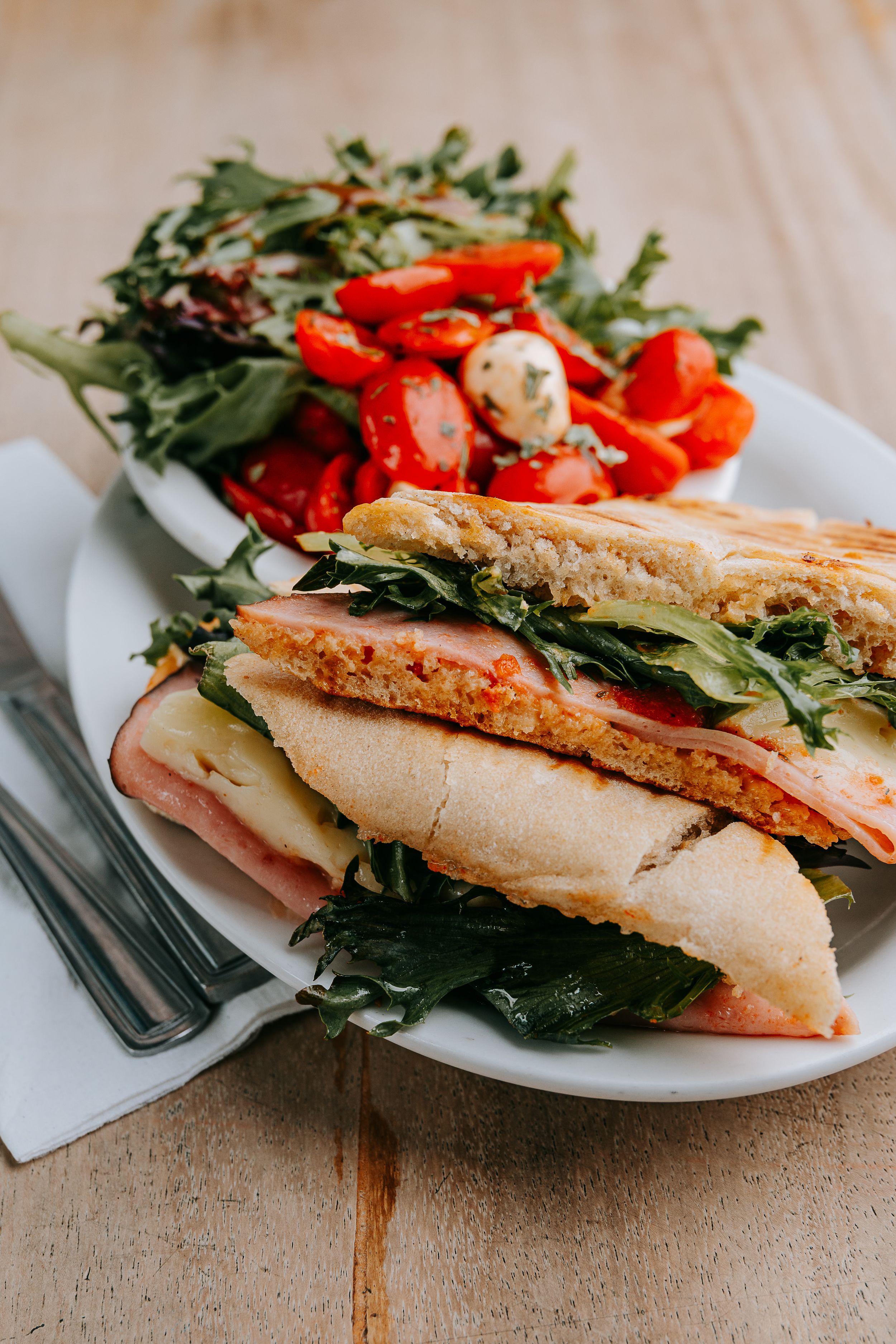 Fresh sandwich with ham, greens, and red peppers served on a white plate.