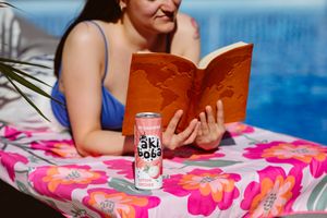 Orange soda can placed next to book on pink floral towel by pool.