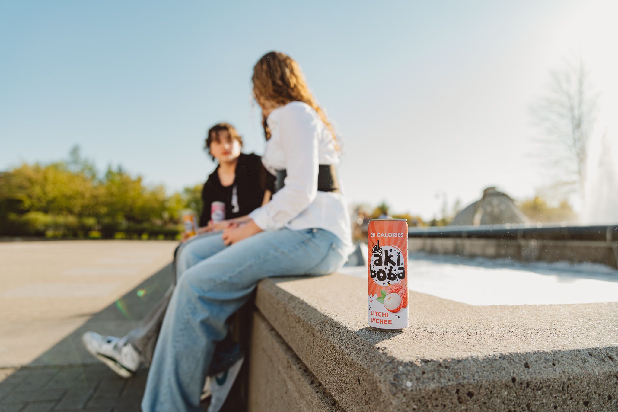 Four cans of orange-flavored Oki Poki sparkling drink lined up on a concrete ledge by the water.