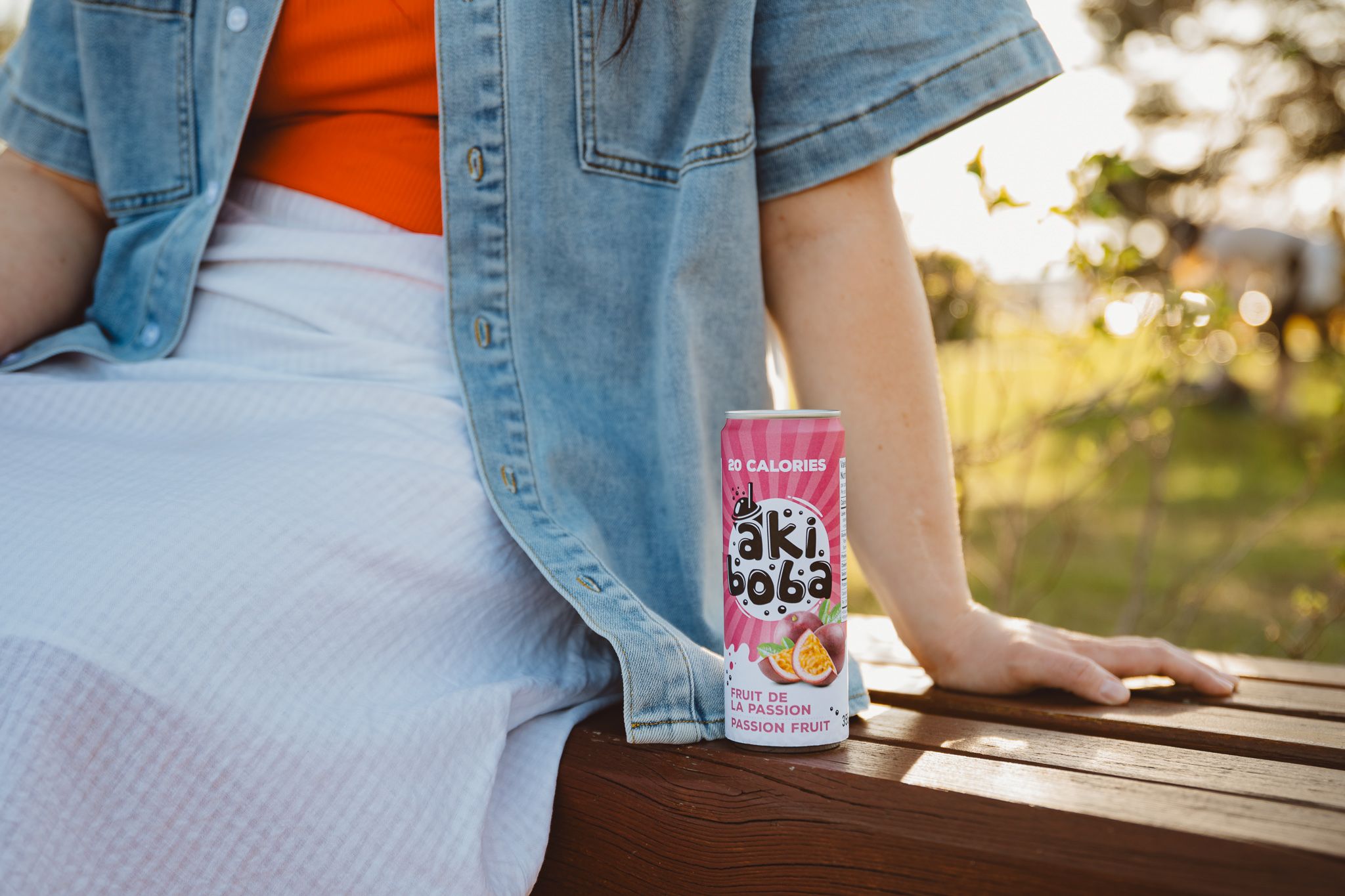 Close-up view of someone wearing denim jacket sitting at outdoor bench with Oki Poki drink.
