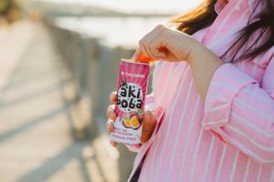 Person in pink striped clothing holding Oki Poki beverage can during golden hour.