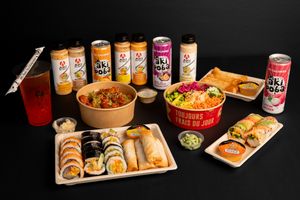 Extensive spread of Asian fusion dishes and Oki Poki drinks arranged on black surface.