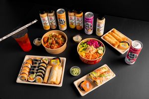 Assorted Japanese sushi rolls and rice bowls with various canned beverages on a dark background.