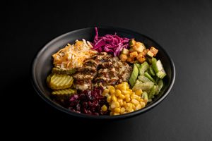 Colorful rice bowl with grilled meat, corn, cabbage, and pickled vegetables in black bowl.