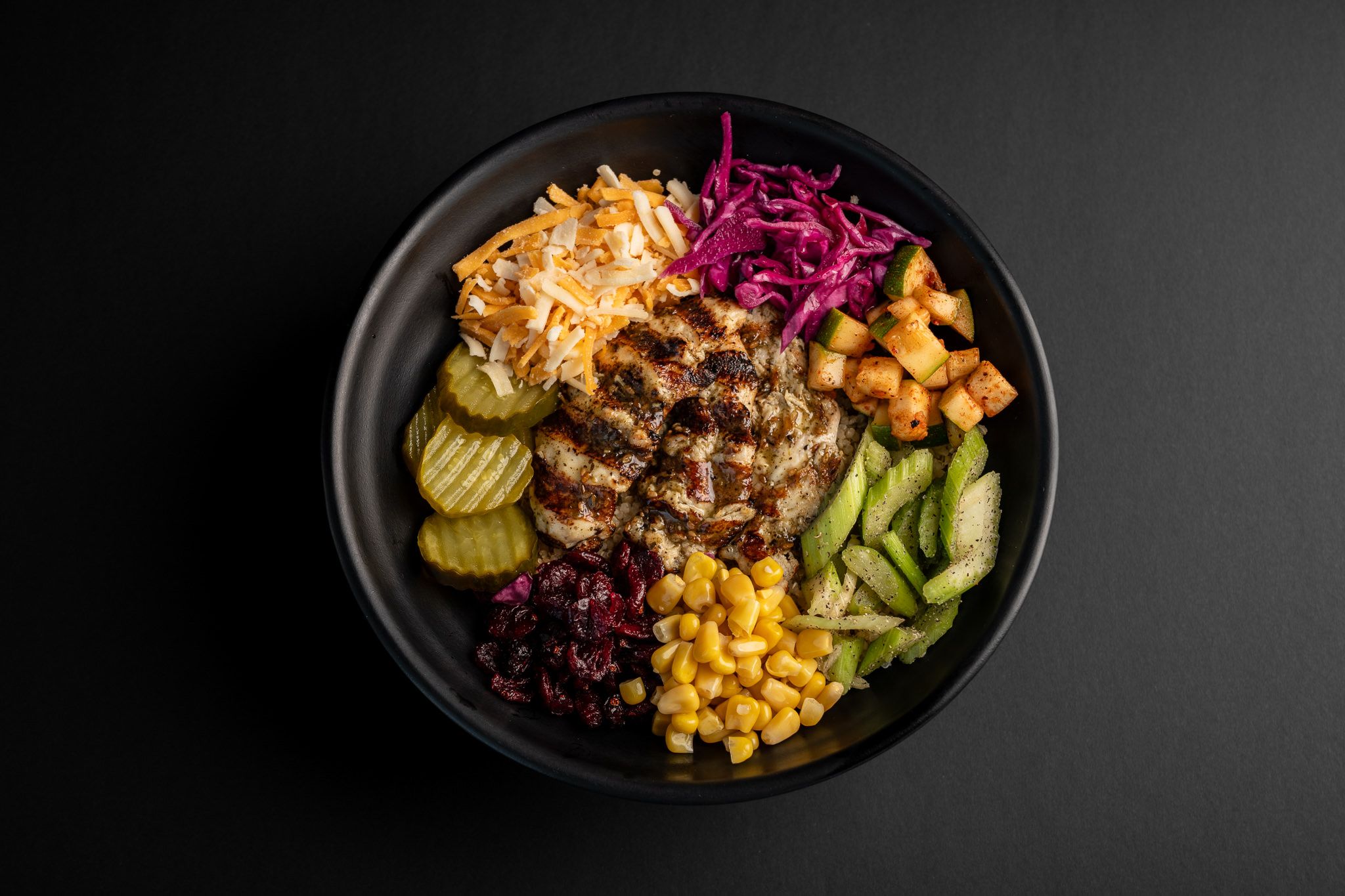 Healthy protein bowl with grilled meat, corn, vegetables and purple cabbage on black plate.