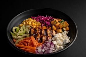 Rice bowl with grilled meat, colorful vegetables, corn, and red onions on black plate.