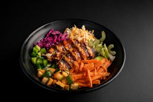 Teriyaki chicken bowl with shredded carrots, purple cabbage, and corn on black plate.