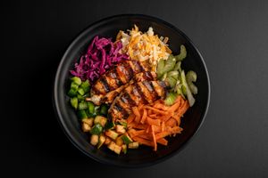 Asian-inspired rice bowl with grilled meat, colorful vegetables and purple cabbage.