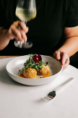 Elegant restaurant dish of crispy arancini with microgreens and edible flowers, served with white wine.