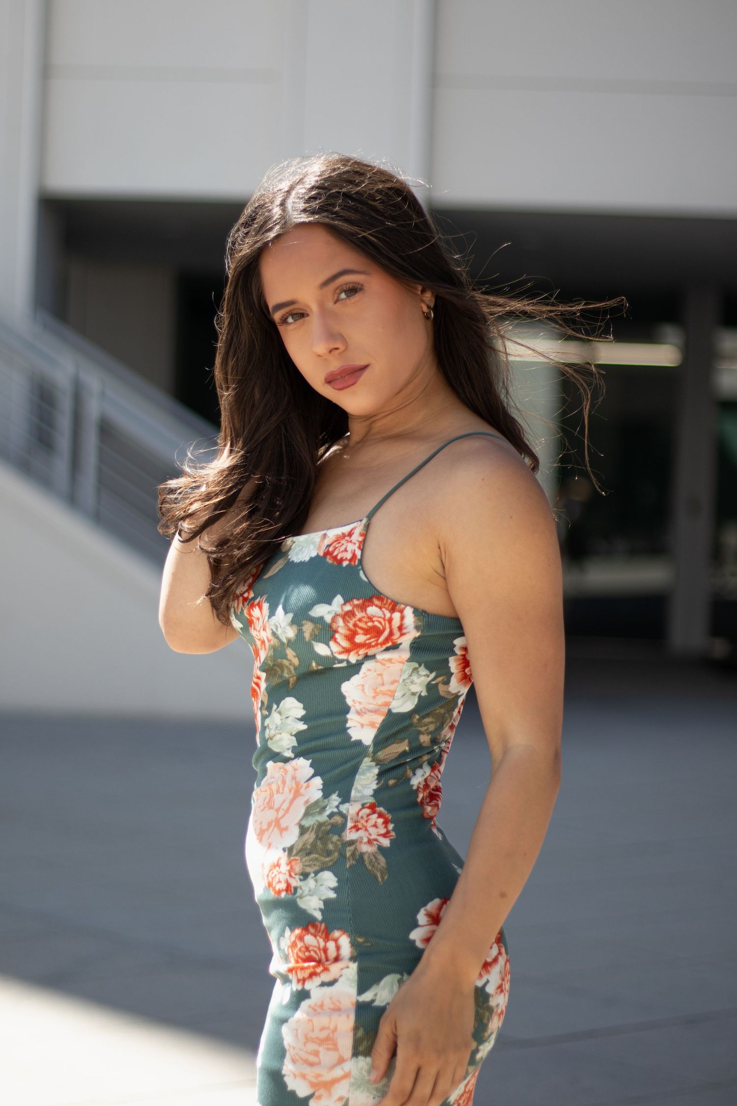 Woman in teal floral dress poses against modern building in outdoor photo series.