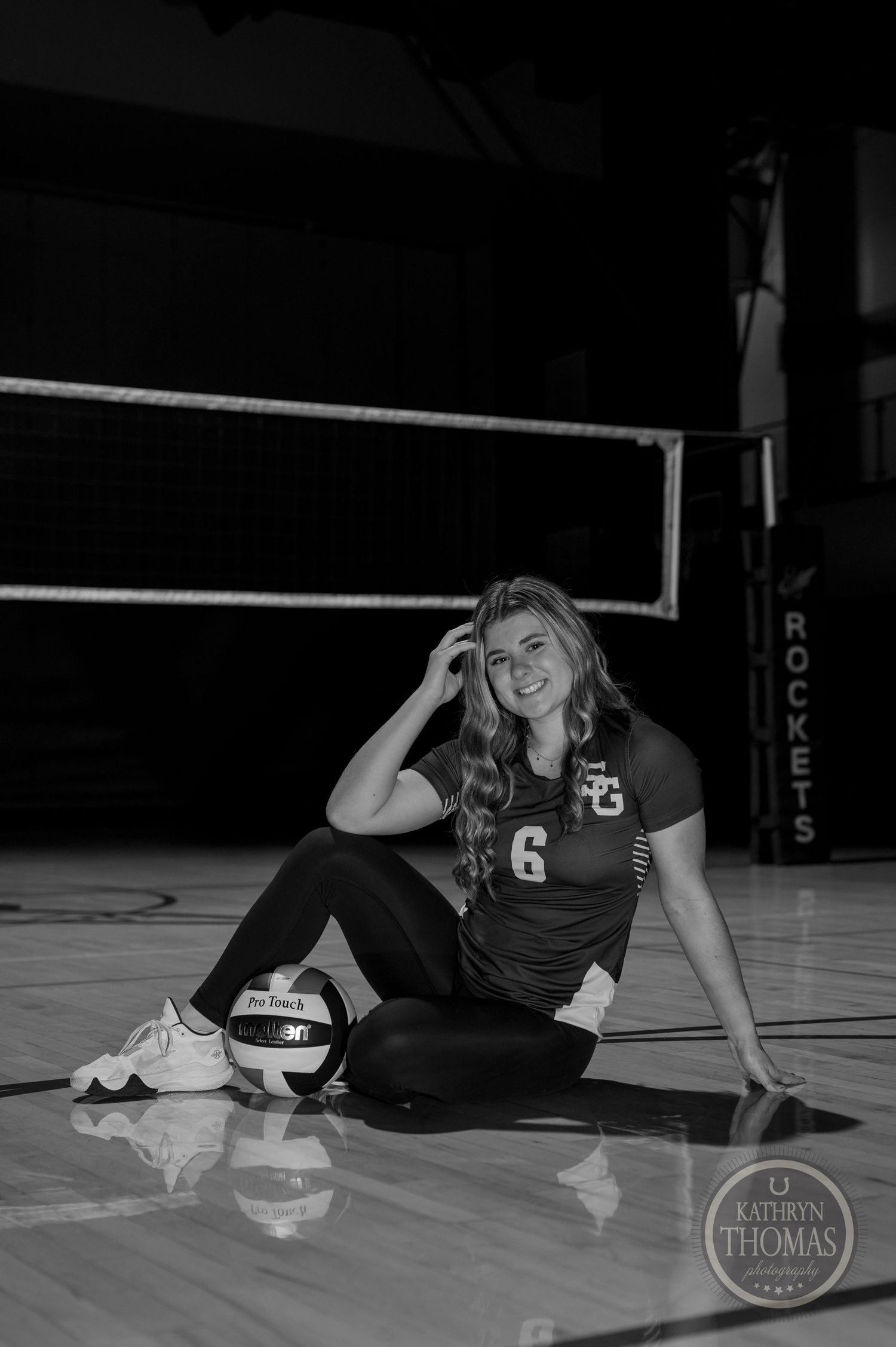 Black and white portrait of volleyball player posing with ball on court floor.