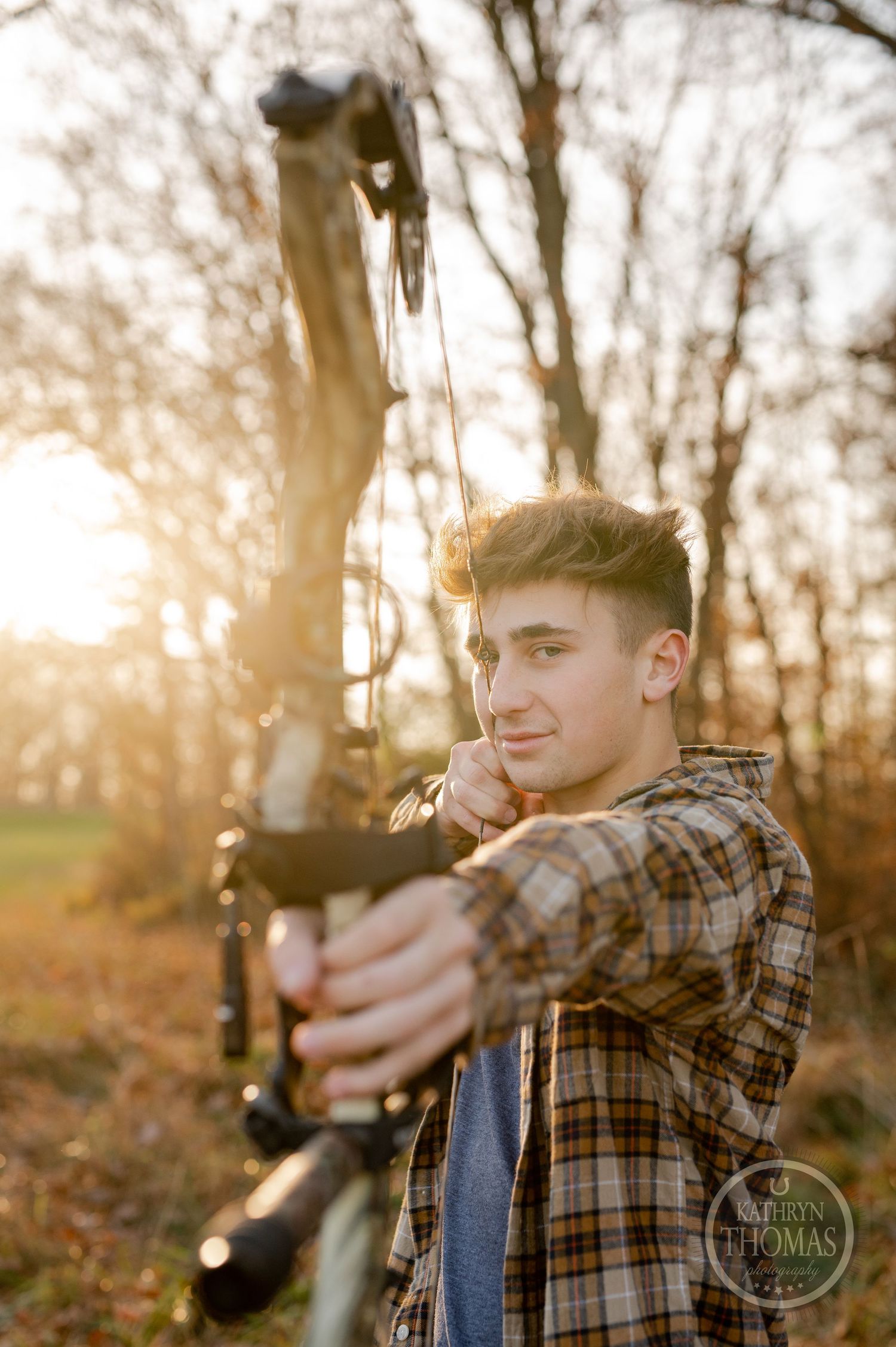 Archer draws compound bow in plaid shirt during golden hour photoshoot.