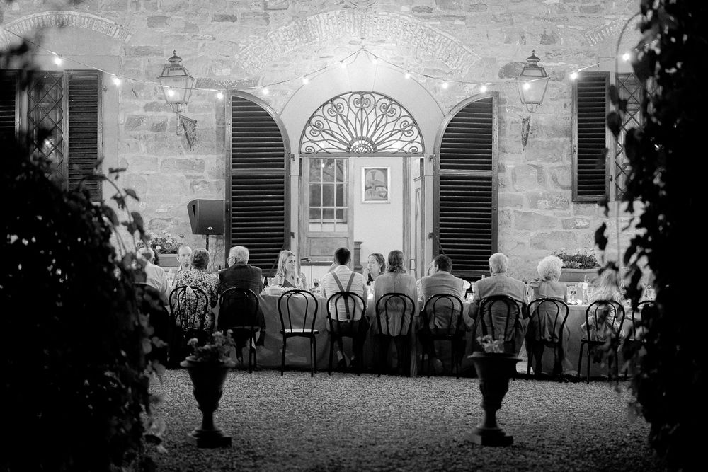 wedding guests enjoying dinner under fairy lights. They're all sitting at a long table, at Borgo Castelvecchi, Tuscany