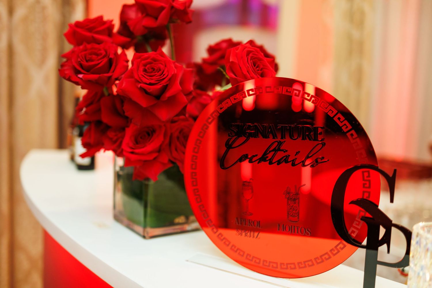 Red roses in square glass vases arranged on a white surface with decorative red accents.