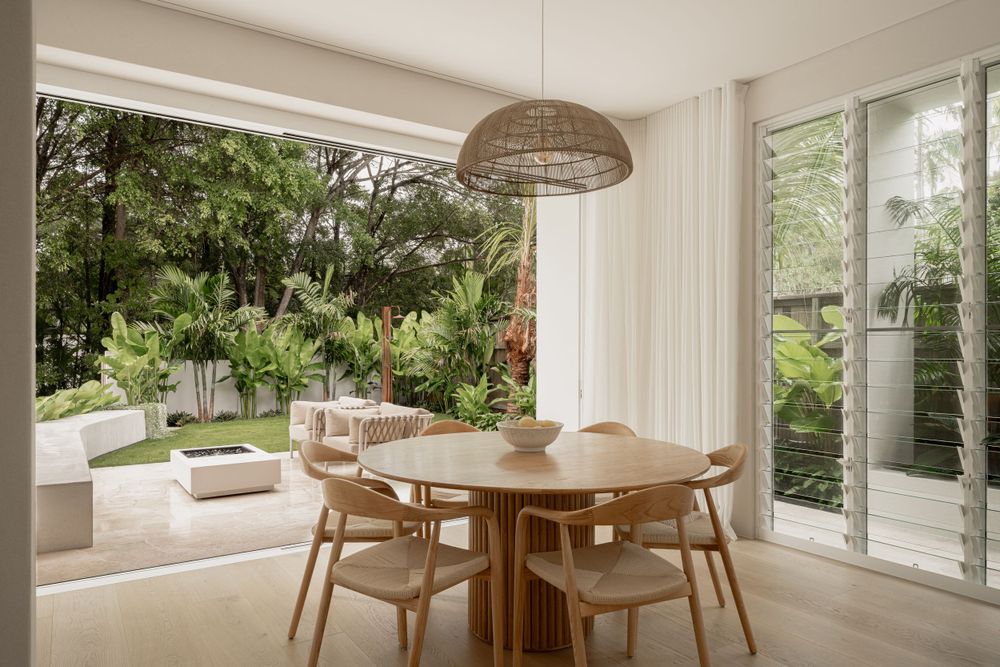 Light-filled dining area with wooden table and woven pendant light overlooking garden views.