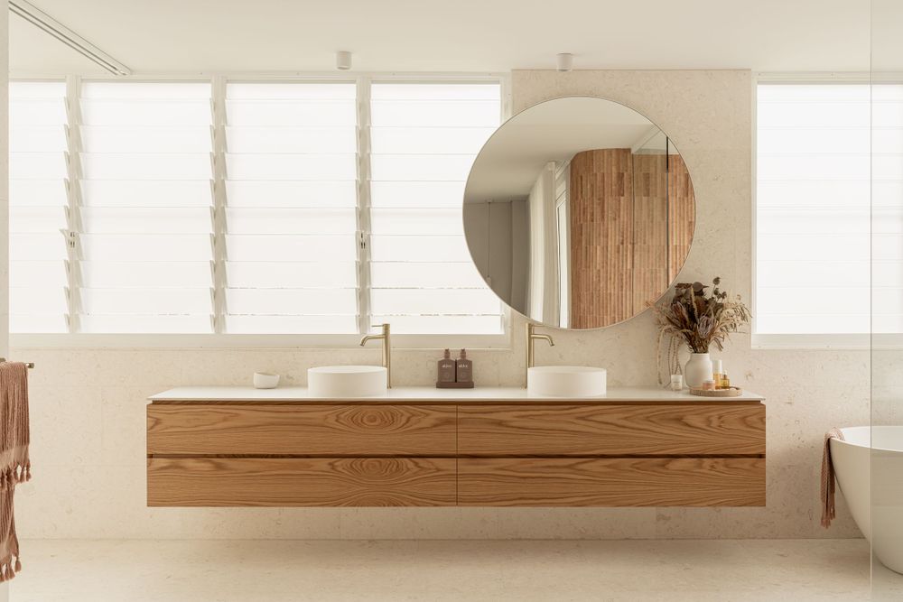 Minimalist bathroom featuring floating wooden vanity and round mirror with natural light.