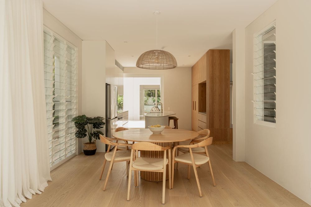 Modern dining space with round wooden table and rattan pendant light in natural tones.