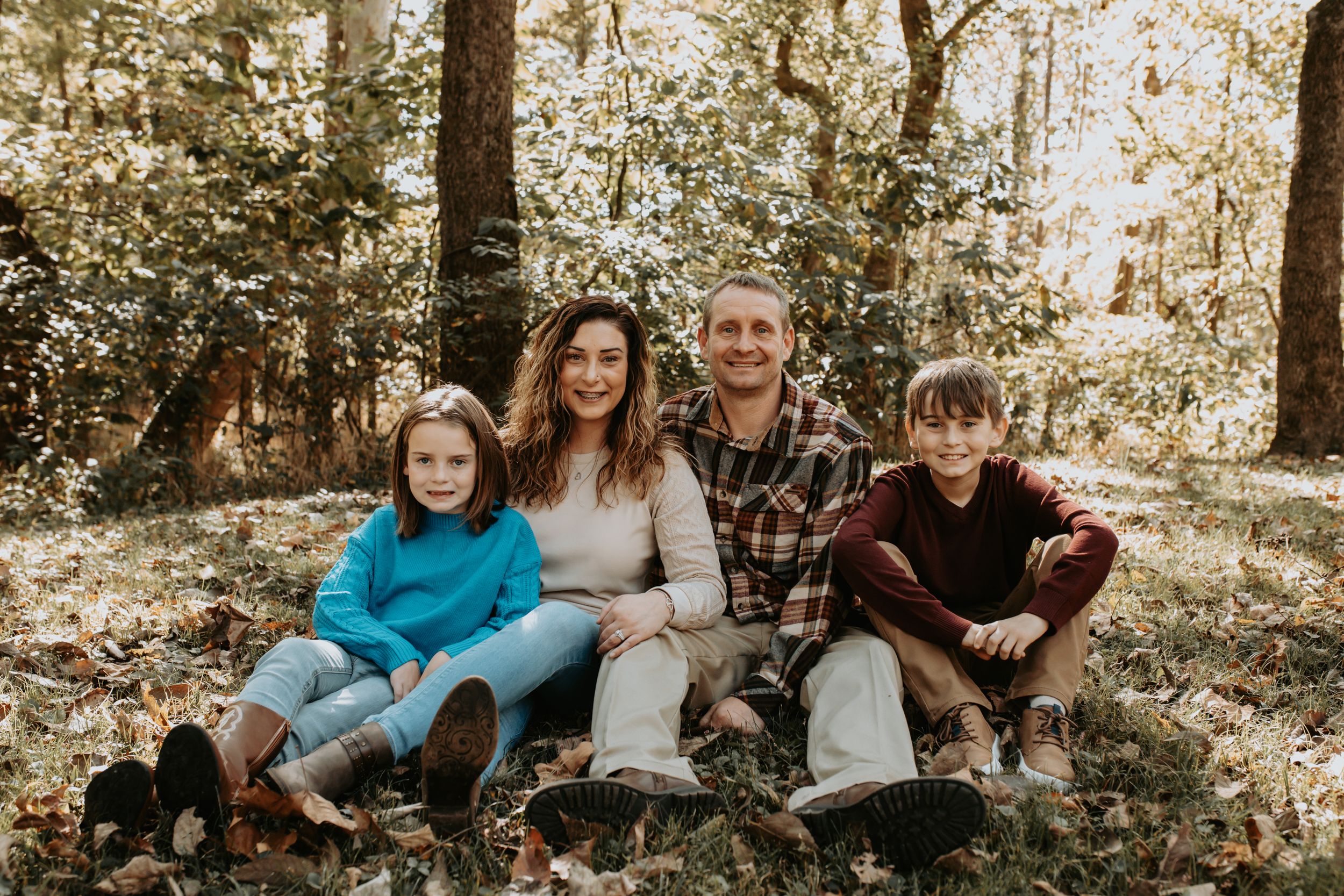 Family relaxing together on fallen leaves in autumn forest setting.