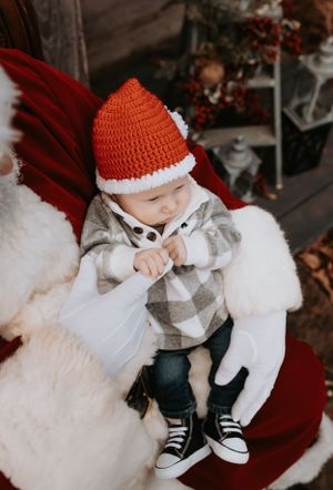 Baby wearing red knit Santa hat and plaid outfit during Christmas photo session.