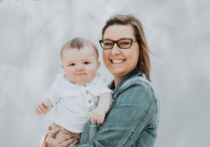 Portrait of parent and baby against light gray background.