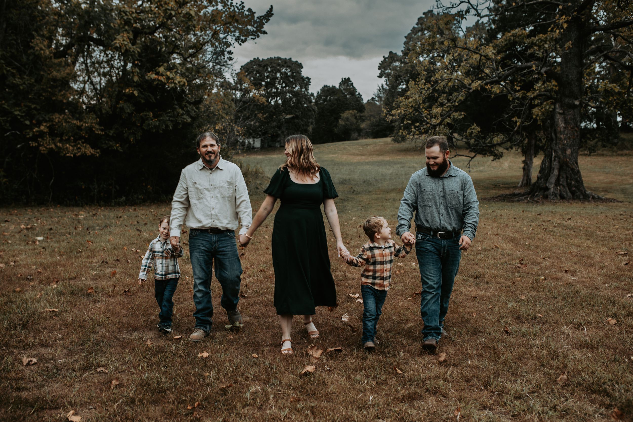 Family walking together across autumn field wearing casual coordinated outfits.
